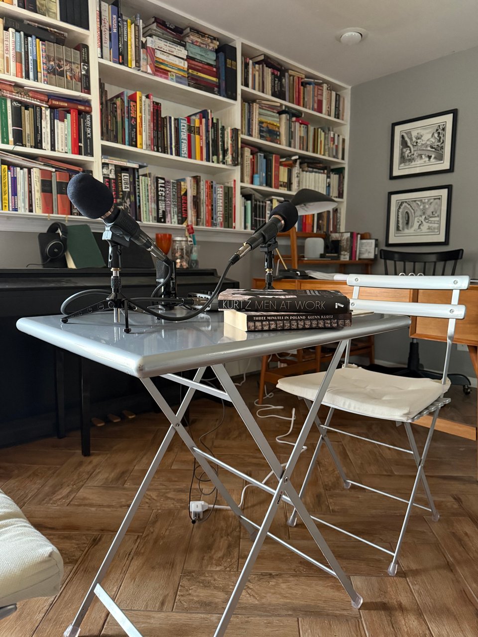 Photo of a silver folding table and two silver folding chairs, with microphones, books, and digital recorders on the table. There are bookshelves the background.