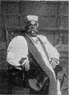 Bishop Holly in a black and white photograph. A black man with a formidable mustache and clerical attire sitting in a chair.
