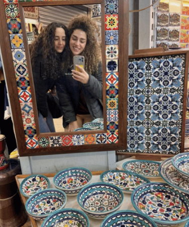Two young women posing for a selfie in front of a mirror with pottery
