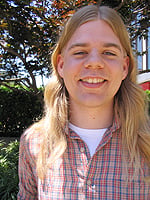 A 23-year-old Lars all smiles, no beard, in a plaid shirt outside of NPR on a sunny day.