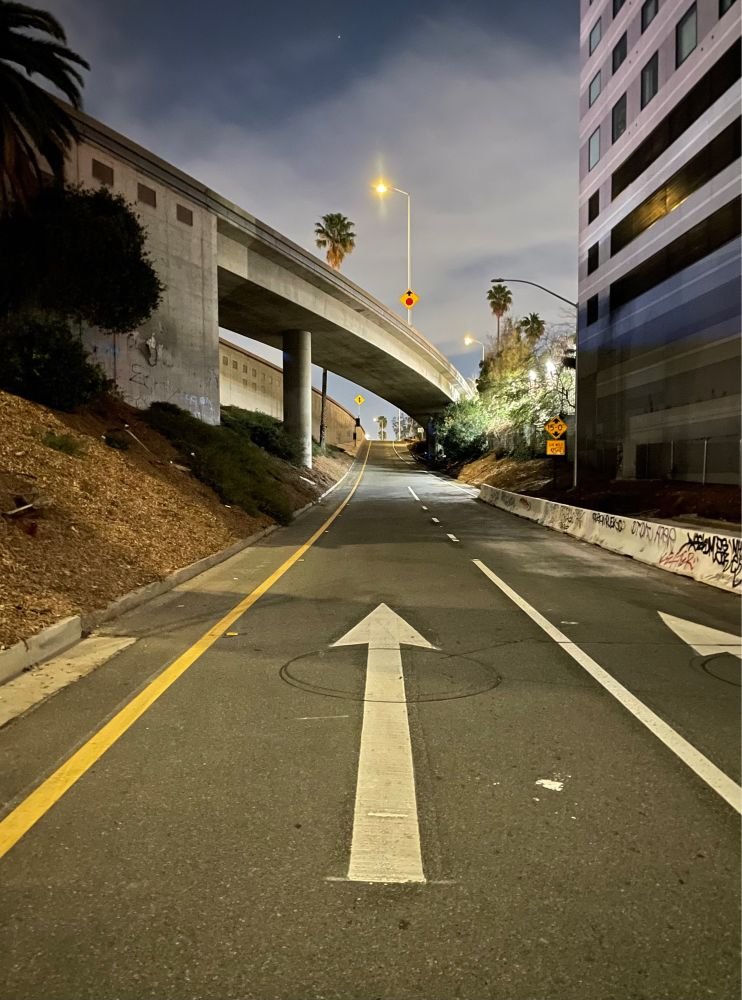 A freeway entrance ramp with a large arrow on the pavement, down the road a bridge curves and a streetlight glows