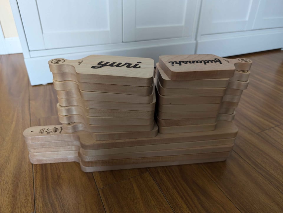 A stack of laser-cut cheese boards. The bottom of the stack is five large “hime”-sized boards. On top of those are two stacks of eight “chibi”-sized boards. The two visible chibi boards say Yuri and Fujoshi.