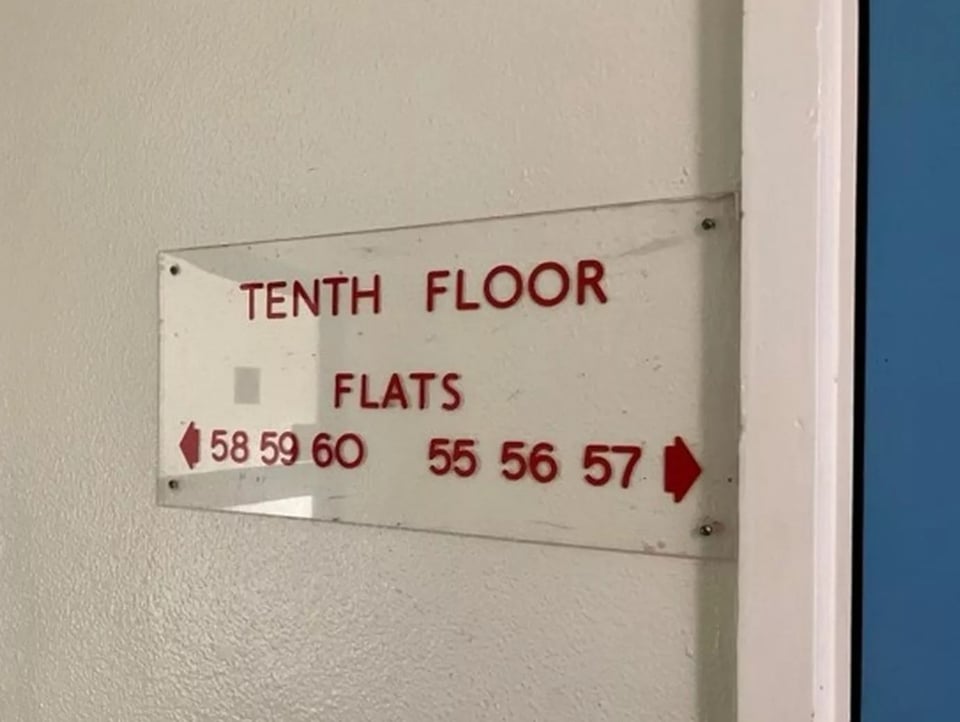 A perspex sign screwed to a wall. It has red numbers and letters on it in a simple san serif font. It indicates it is on the tenth floor, and which way to go to which number flat