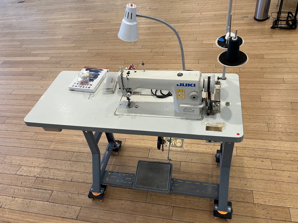 A sewing machine sits on a table next to some thread and other sewing supplies.