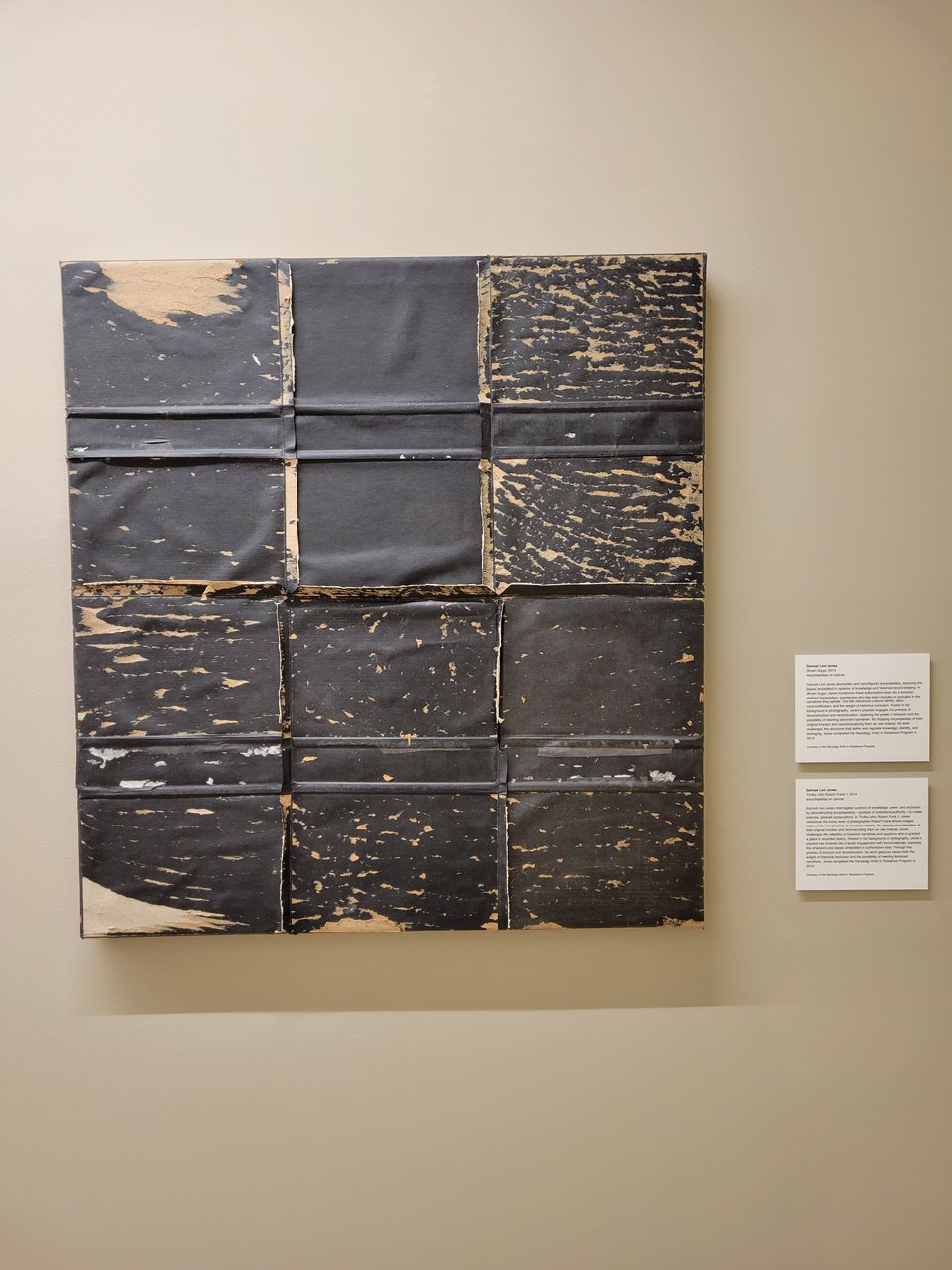 Brown Sugar (2014) by Samuel Levi Jones. This looks like a large grid of black cardboard-esque paper, where some of the paper is torn away in a splatter-like fashion to reveal the cardboard brown underneath. This is made from stripped-apart encyclopedias on canvas and is commentary on the bias of points of reference and authority, since there was a time when encyclopedias were considered a respectable source of truth. This piece questions who has been included or excluded in the narratives upheld by systems of knowledge and historical record-keeping.