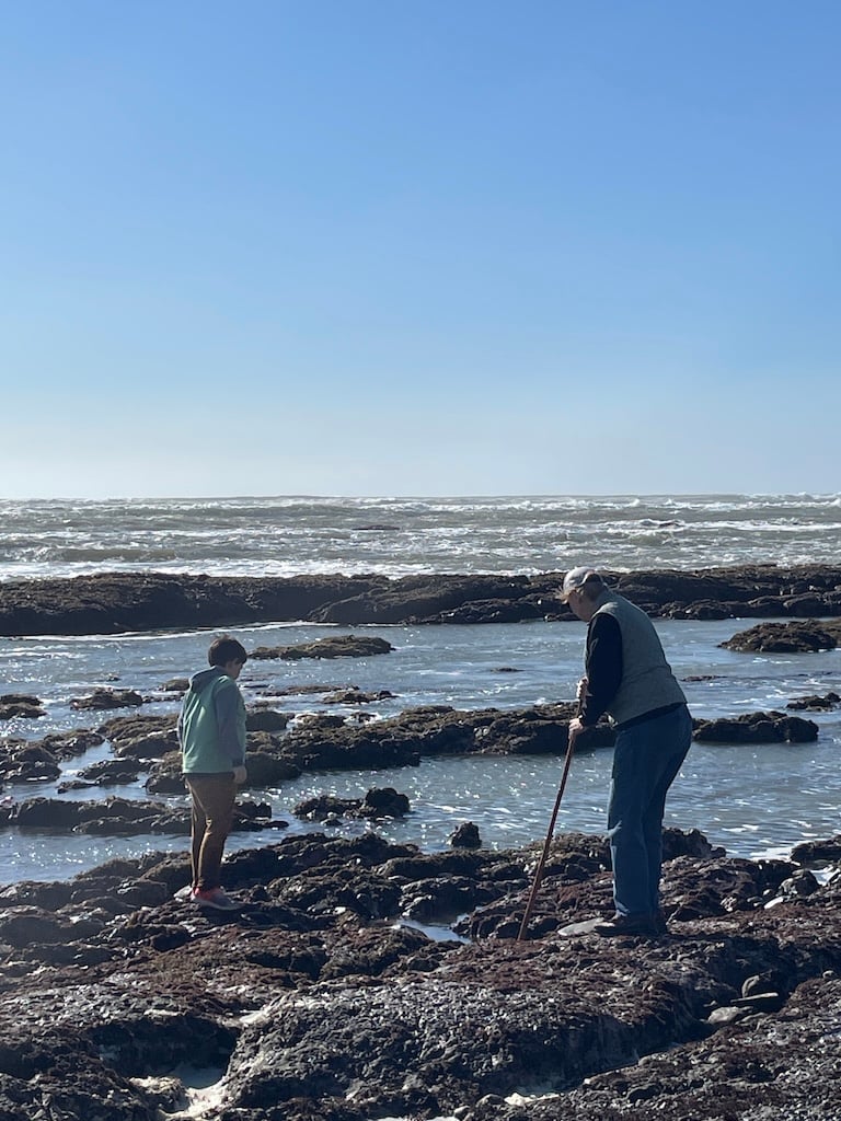 A young boy and his grandmother walk along the tide pools while the ocean froths behind them.