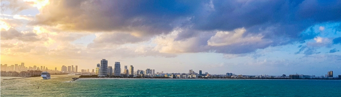 The coastline of Miami with clouds over it, some of which are yellow from the sun