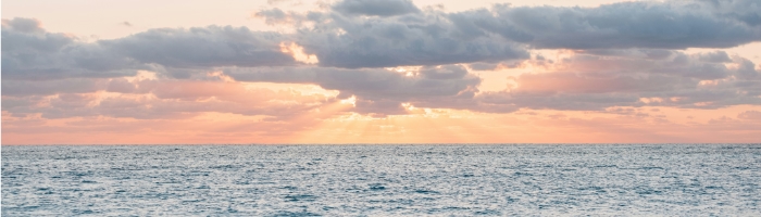 the sun setting over the ocean behind clouds