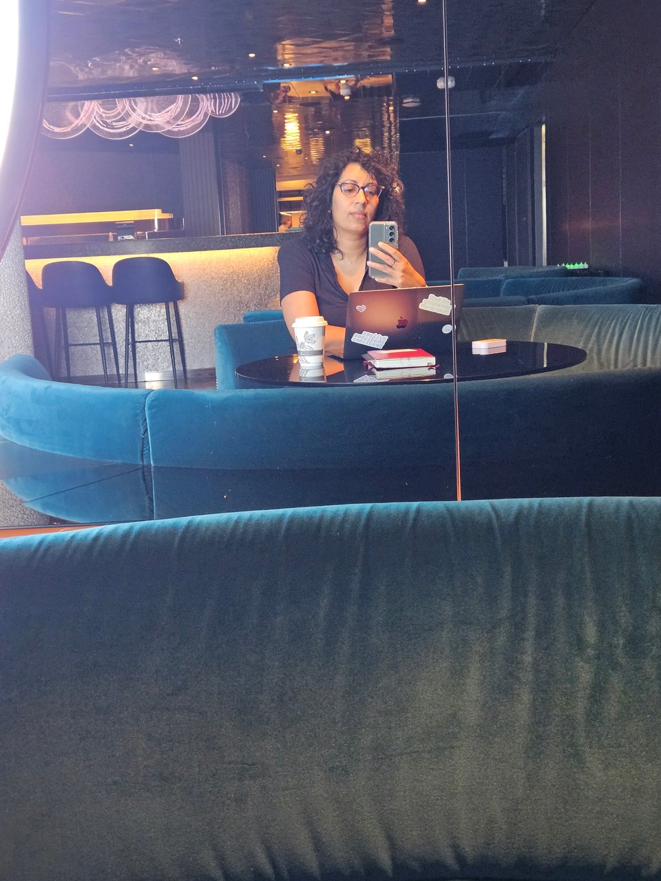Renee sitting in on a velvet couch, taking a picture in the mirror. Her laptop is open in front of her.