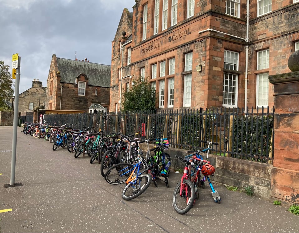 Over twenty children's cycles and a smattering of kick-scooters are locked to black sheffield stand cycle racks outside of the red bricked Roseburn Primary School - a riot of colour on an otherwise overcast day.