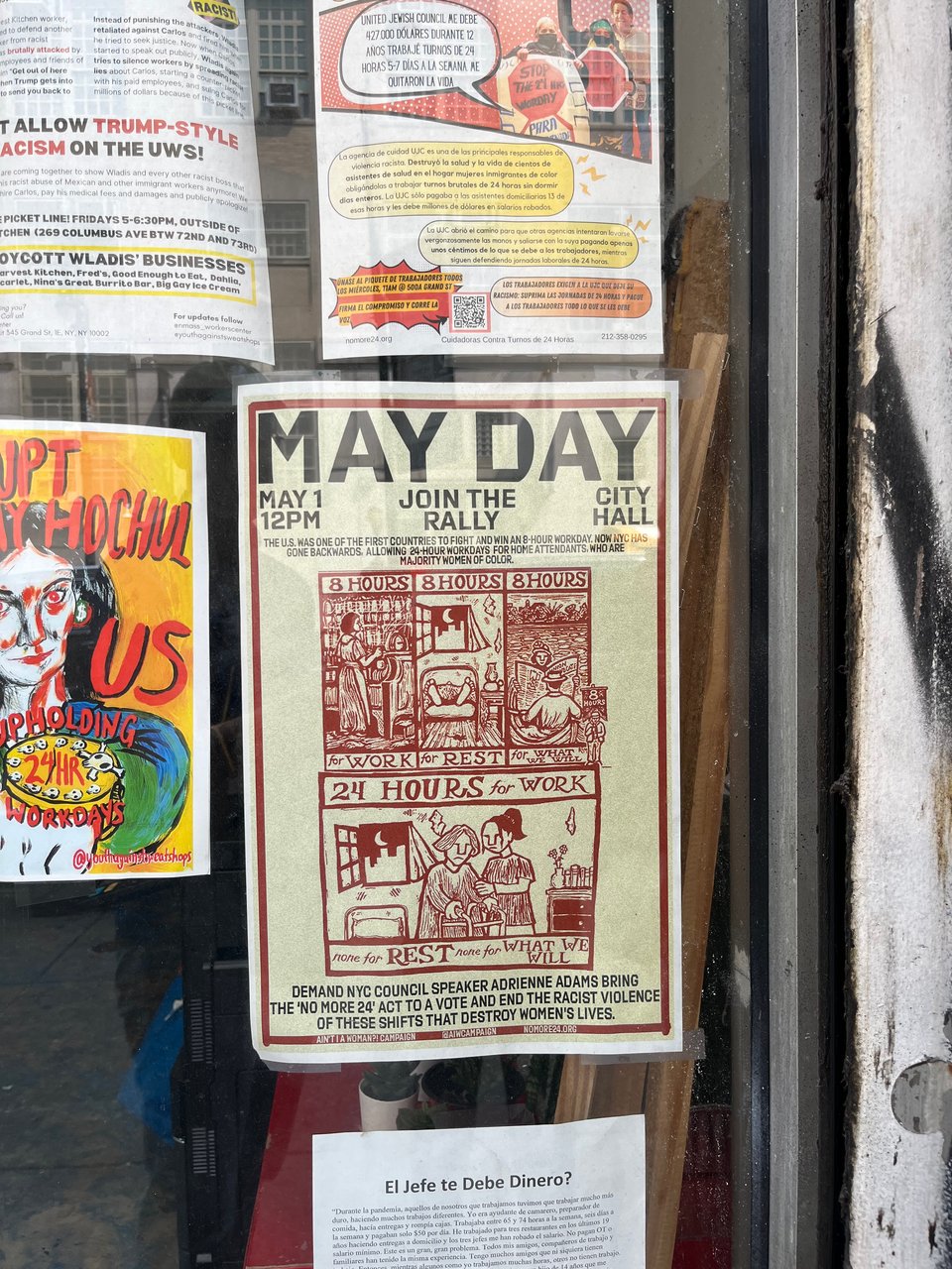 A storefront with a May Day rally poster taped to the inside of the window. The poster uses Jesse Ragan's typeface Export.