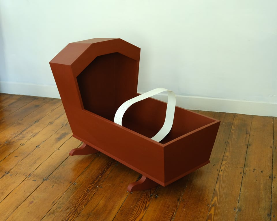 A reddish cradle music box sculpture with a strip of paper inside.