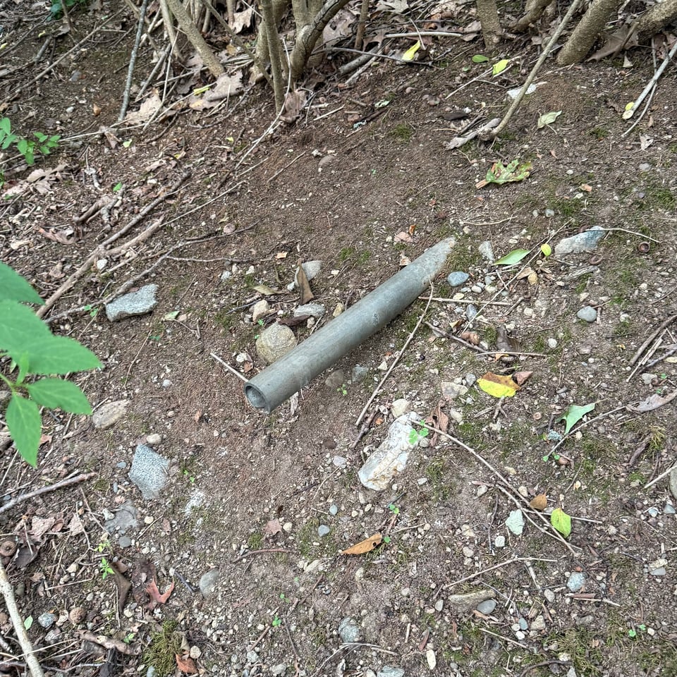 photo of a metal pipe sticking horizontally out of an incline in the ground, with forsythia growing nearby