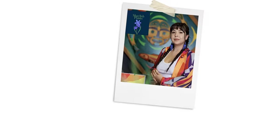 A polaroid style photo of an Indigenous woman looking at the camera, her hair in braids, wearing beaded earrings and a colorful shirt.