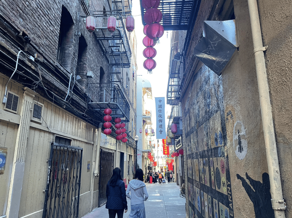 another alley in Chinatown with hanging red lanterns, murals, and banners with Chinese characters