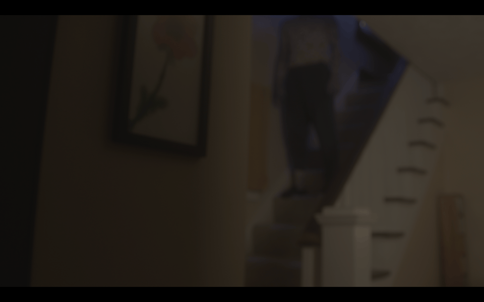 A blurry image of a figure on a set of stairs in a living room, their head obscured