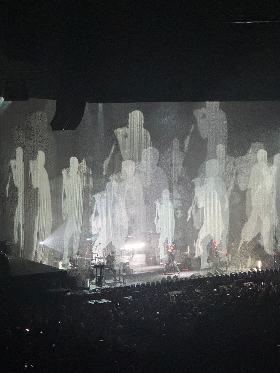 Nine Inch Nails performs on a stage surrounded by silhouettes of Trent Reznor.