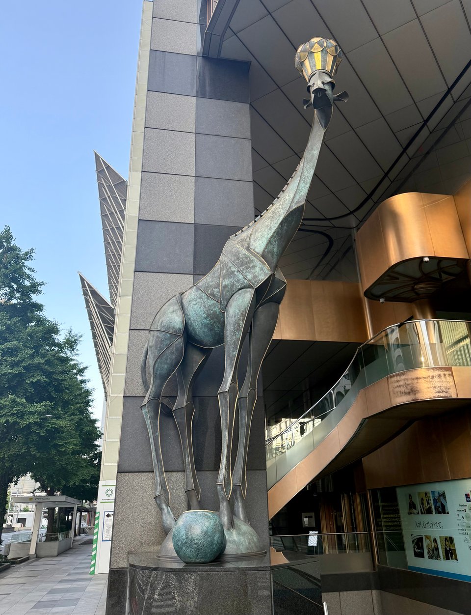 photo from Ginza of a metal statue of a giraffe wearing a crown, in front of a business building