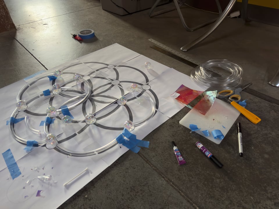 Seed of life made out of vinyl tubing on floor with various materials—scissors, glue, markers, rulers, and tape.