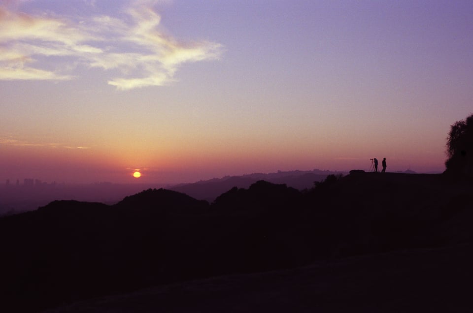 a photo of sunset at griffith park, looking west towards the pacific ocean. Two people are silhouetted in the distance. 