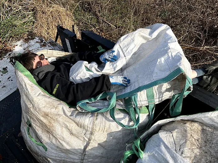 [Cortney resting on top of an enormous bag full of, presumably, other bags. Two additional bags cover her like a blanket.