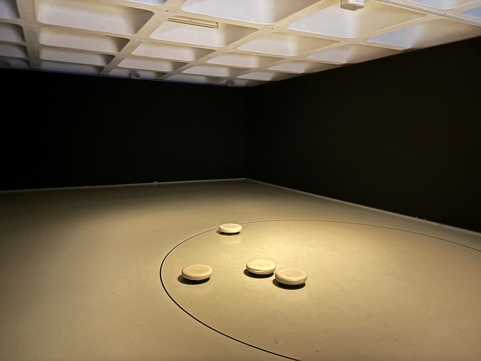 A large darkish room with a circle inscribed on the flat ground, and four tiny wheeled stools, maybe four inches high