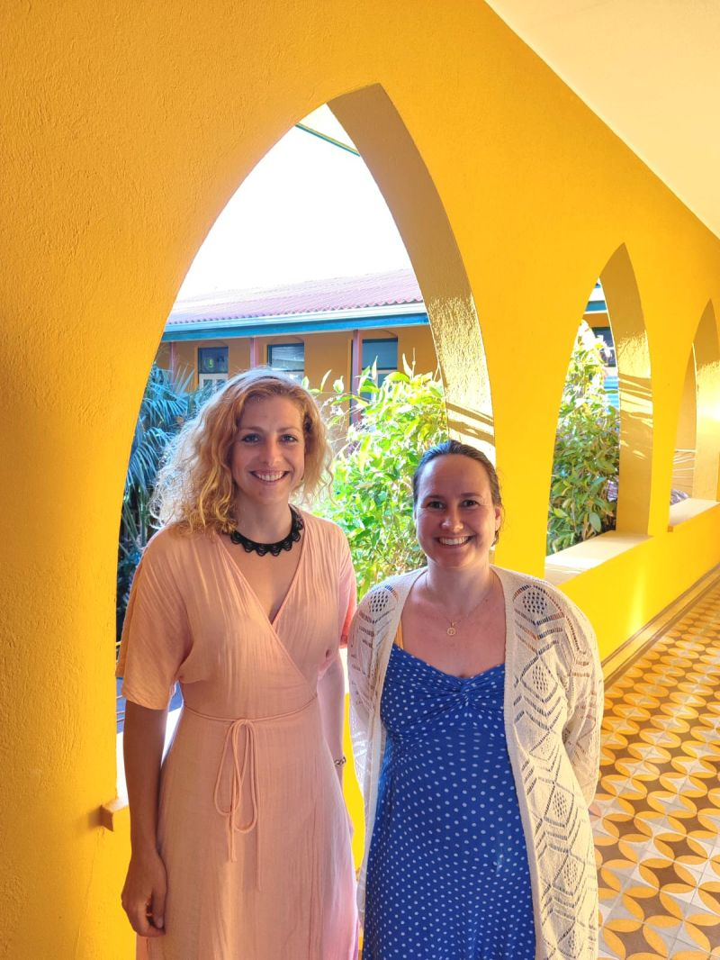 A picture of Hannah Meijer (left) and Brechtje Huiskes at the University of Aruba, de la Salle building. Both are wearing beautiful dresses and are smiling happily into the camera.