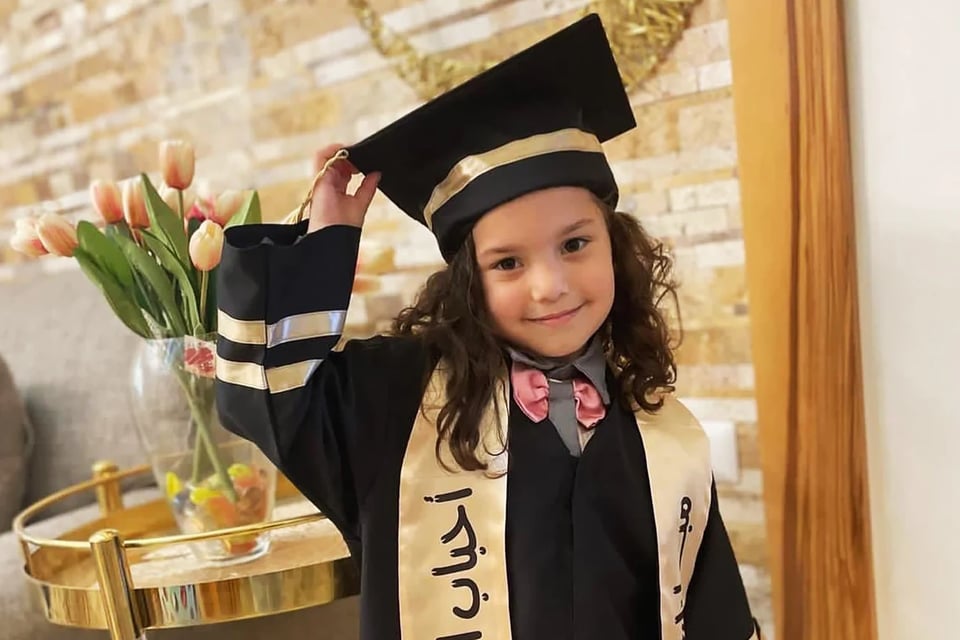Hind Rajab in her preschool graduation gown and cap. She smiles for the camera. A bouquet of tulips is behind her.