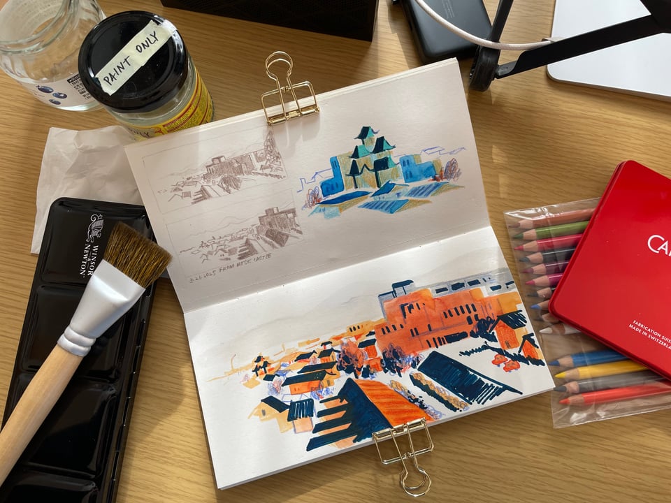 Sketches of a cityscape. The materials used to create it are scattered around.