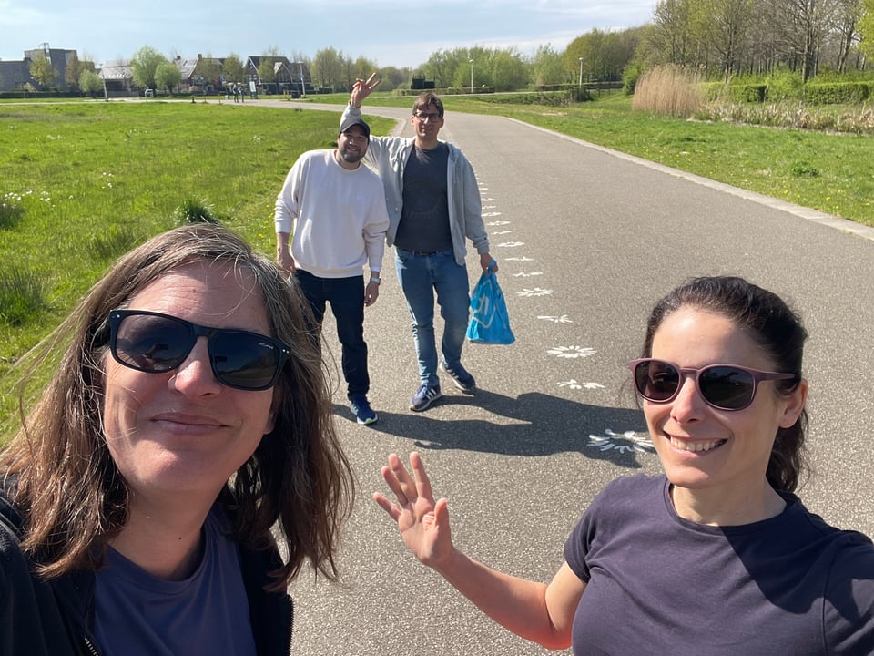 Two women smile at the camera and two men wave behind as they all walk in the park.