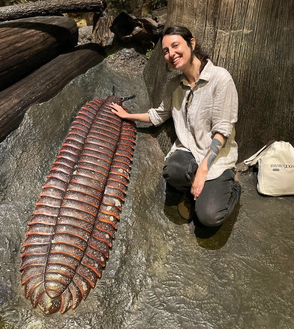 Science fiction and fantasy author T. K. Rex poses elatedly with a lifelike replica of the giant Carboniferous stem-millipede Arthropleura, giving it a gentle pat because it is a good bug. (Not a true bug though.)