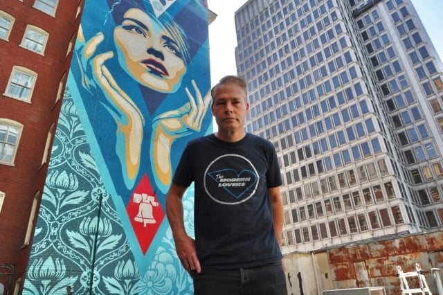 Shepard Fairey stands on a rooftop beside his new mural, ”Uplift Justice.” (Emma Lee/WHYY)