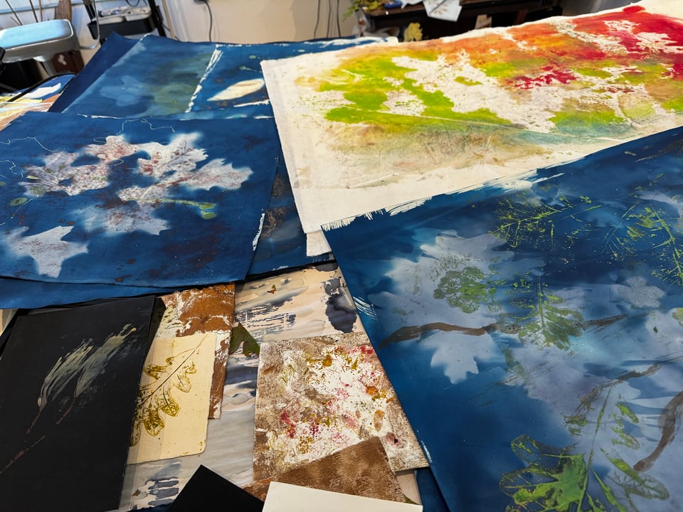 Group of artist prints - mixture of brightly colored cyanotypes and encaustic monotypes on studio table.
