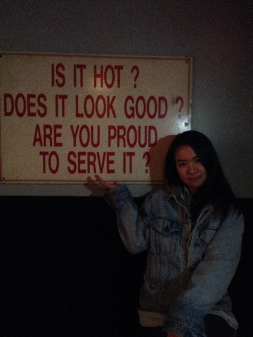 The indie musician Mitski poses in front of a sign that reads, "Is it hot? Does it look good? Are you proud to serve it?"