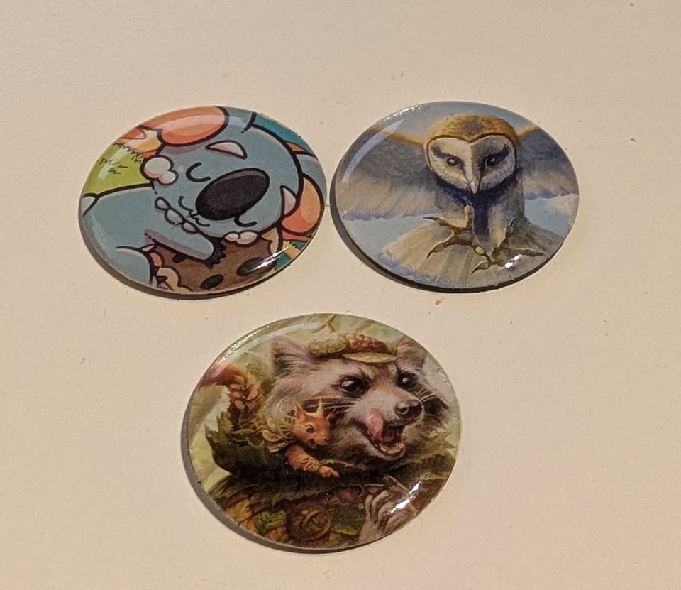 Three small one inch tokens with Komala the Pokemon and and an owl and a raccoon from Magic the Gathering.