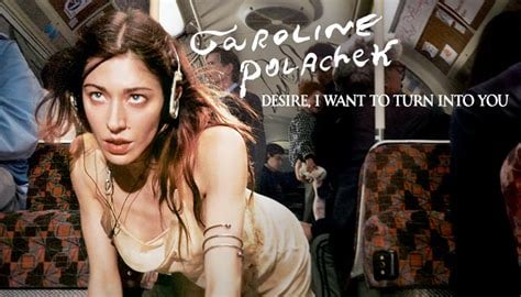 A woman with long brown hair, wearing a light-colored slip dress and headphones, is pictured on what appears to be a bus or train. She is leaning forward with her head tilted back, looking up towards the viewer with a slightly intense expression. Her left arm is visible, adorned with several thin bracelets. The background is blurred but shows other passengers and the interior of the vehicle. The words "CAROLINE POLACHEK" and "DESIRE, I WANT TO TURN INTO YOU" are written in a stylized font across the top right of the image.