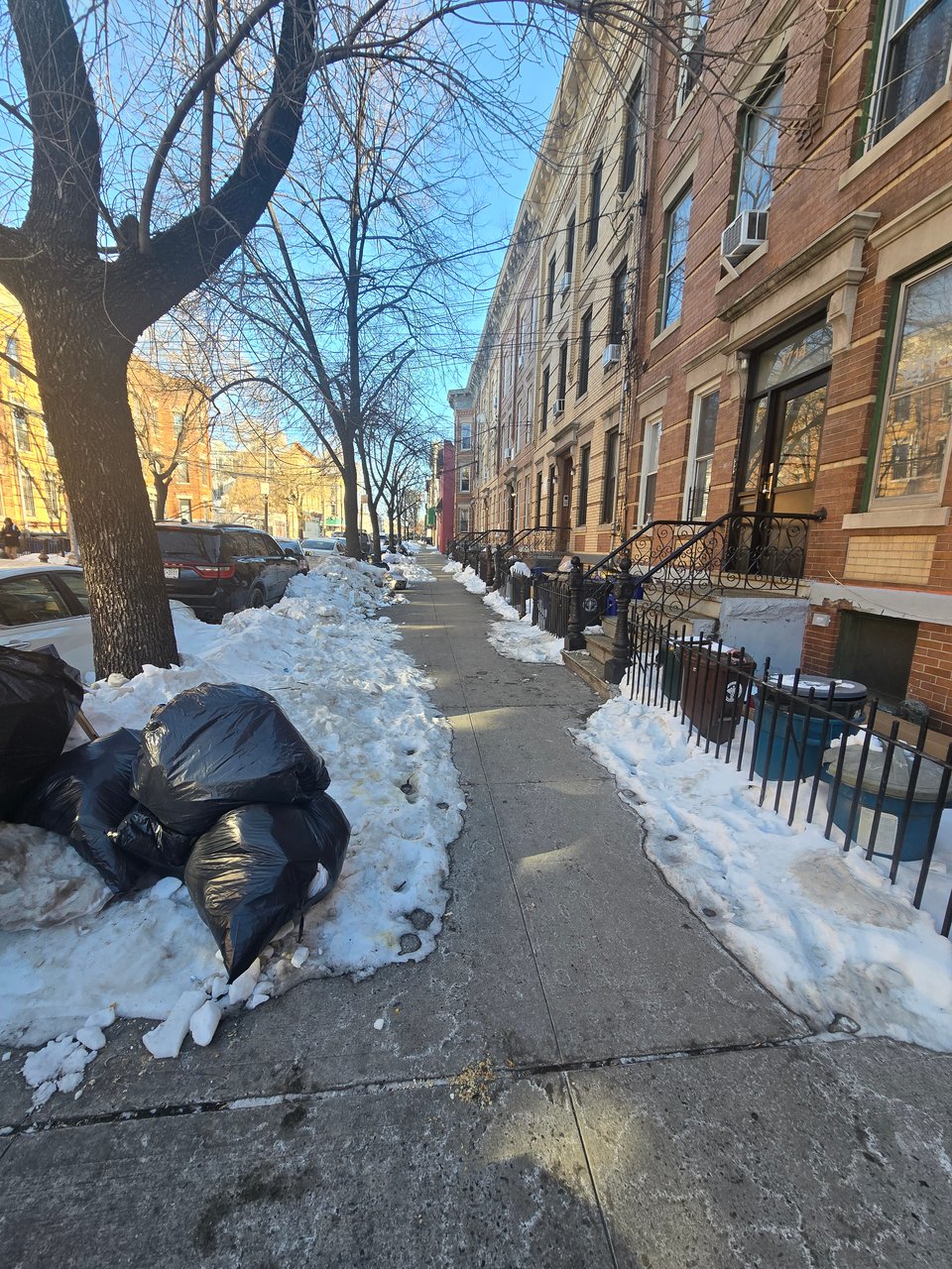 A photo of garbage bags on top of a hill of snow on a New York City street.