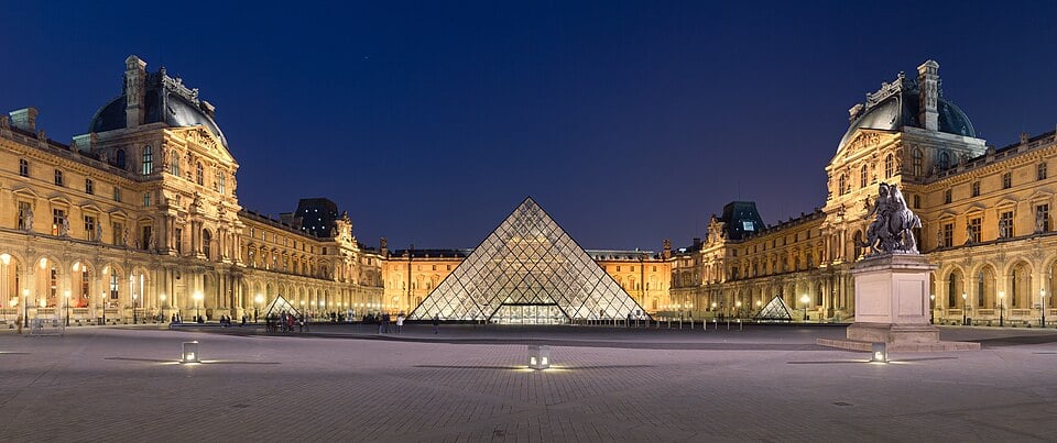 A courtyard with old buildings on all sides of a glass pyramid