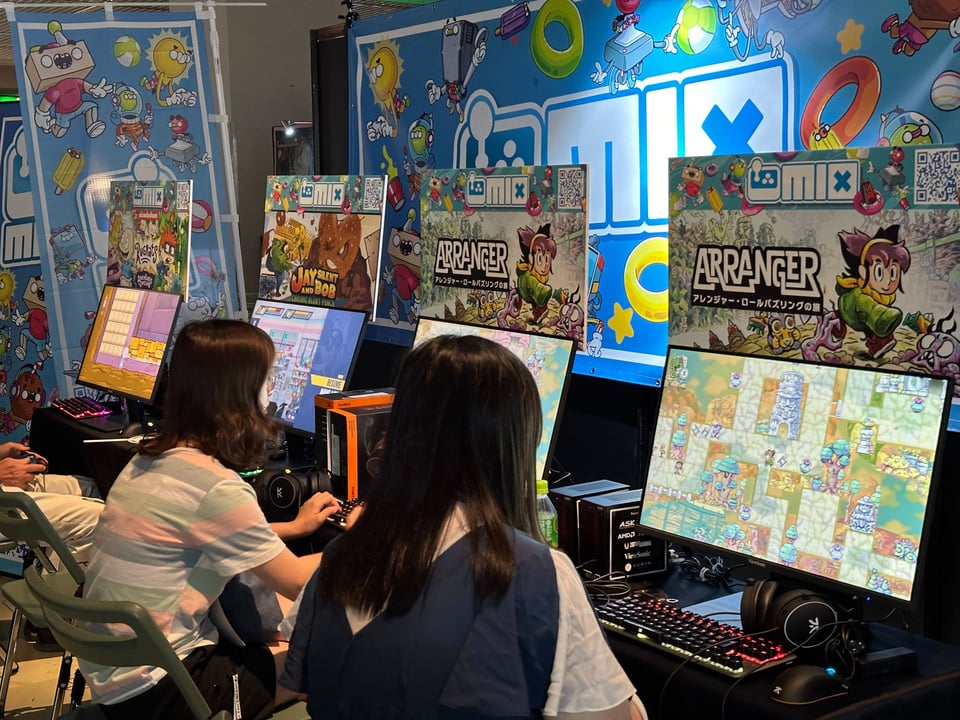 Two people playing the game on computers in a colorful booth at BitSummit