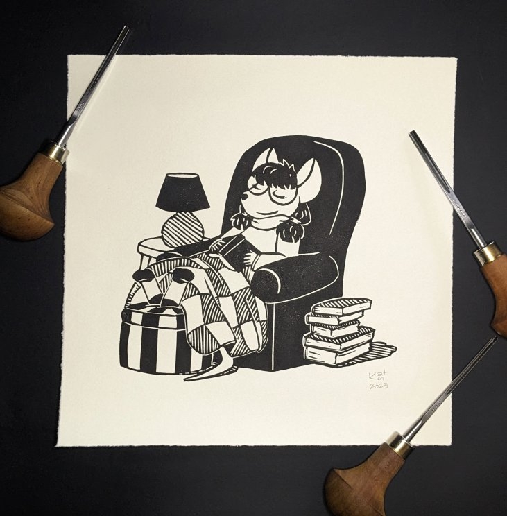 photo of a block print. the block print is in black ink on white paper and is of a cozy little mouse girl, in a comfy chair with her feet on a striped ottoman, fast asleep under her book and a patchwork quilt. there's a giant pile of books on the floor next to the chair, waiting to be read.