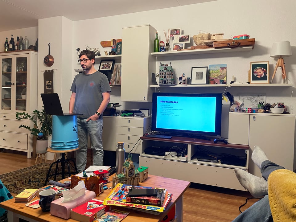 A man stands in front of a computer in a living room as he practices a talk.
