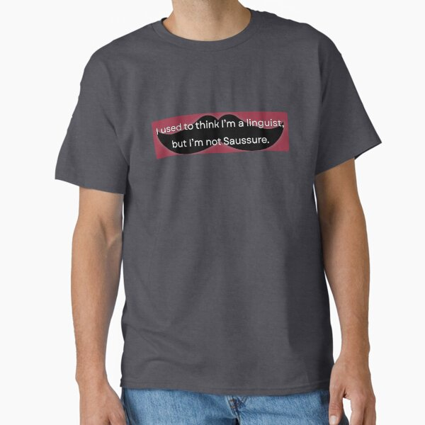 A catalogue image of a grey t-shirt on a male-presenting body, on which is printed (the t-shirt, not the body) a black hipster moustache design on reddish background, reading, in white sans serif print 'I used to think I'm a linguist, but I'm not Saussure'