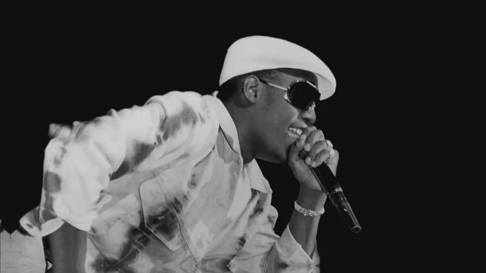 Kool Moe Dee rapping on stage in a track suit and kangol