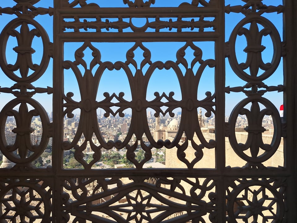 Picture of a metal gate, city visible through the gaps
