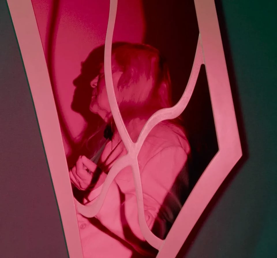 a man seated in front of a crooked window in red light