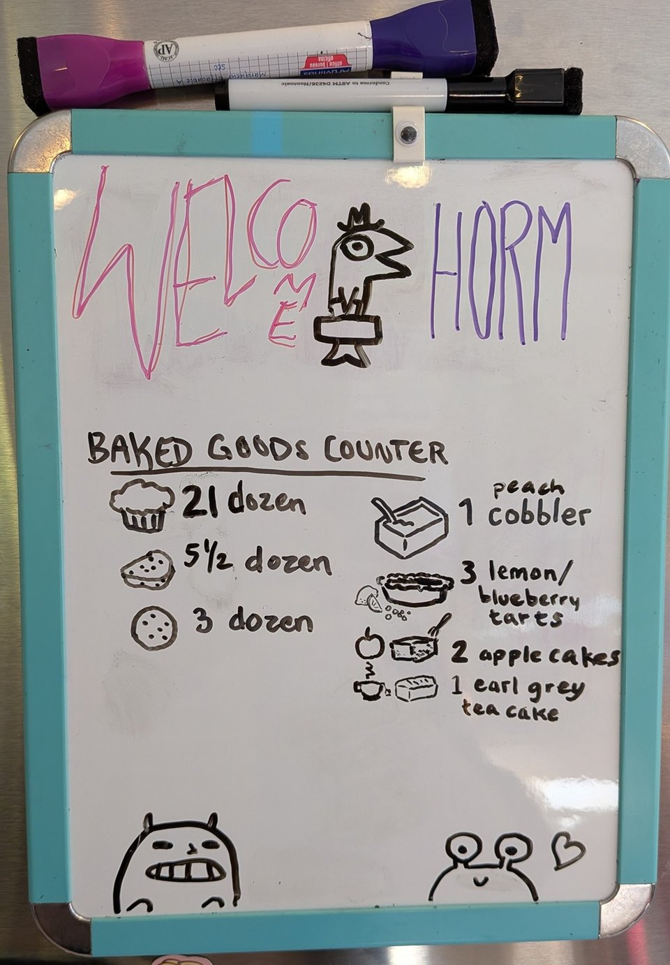 a small whiteboard. Monsters are drawn at the bottom and the top says Welcome Horm with a fish carrying a briefcase and wearing a jaunty hat. The stats are: 21 dozen muffins, 5 1/2 dozen scones, 3 dozen cookies, 1 peach cobbler, 3 lemon/blueberry tarts, 2 apple cakes, 1 earl grey tea cake