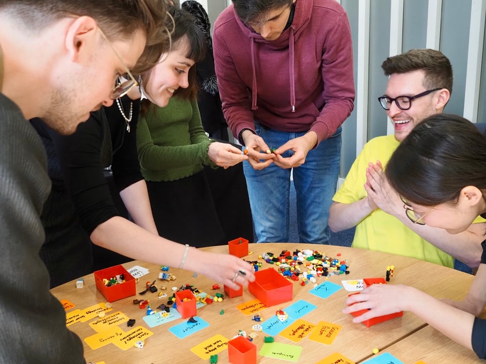 Five people around a table playing with LEGO and cards