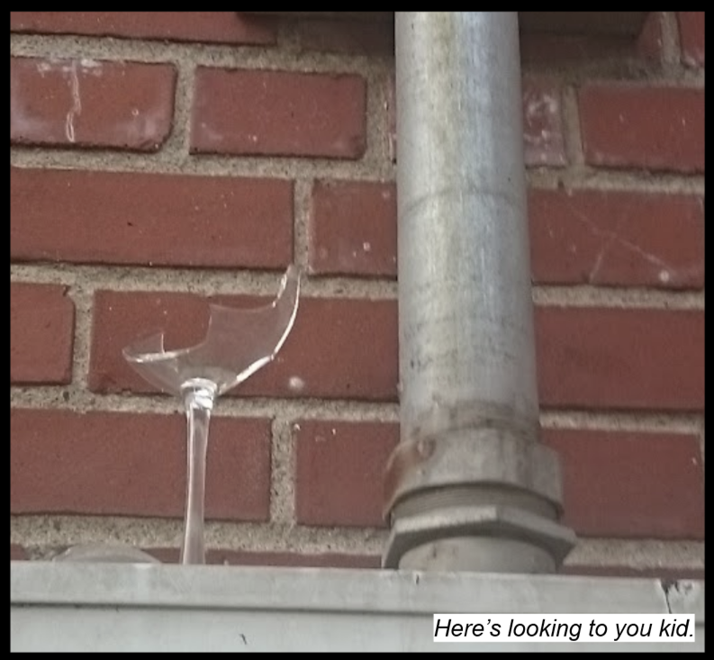 A broken win glass on top of an electric box affixed to a brick wall. Text reads: "Here's looking to you kid."