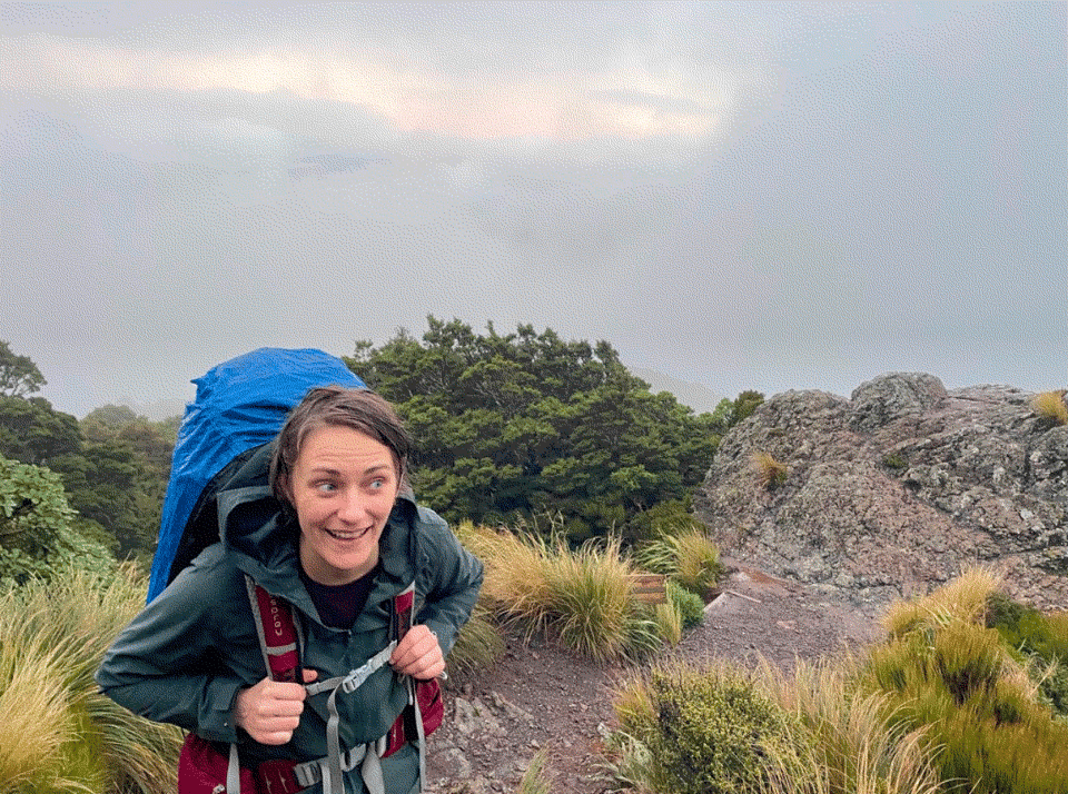 Ember hiking with a rain-covered backpack and making sort of a funny happy face.