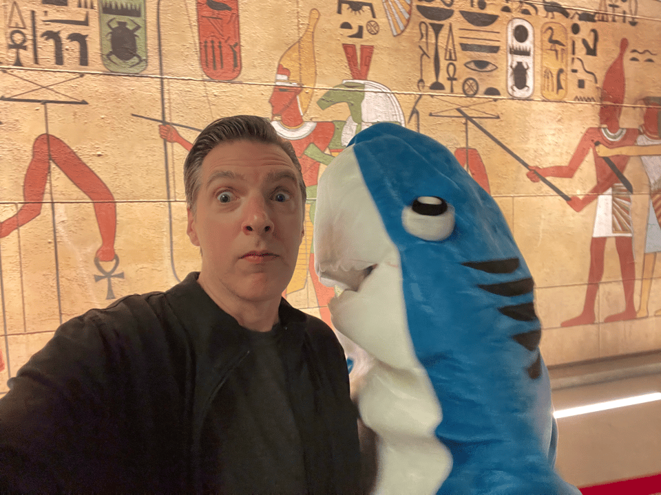 A person in a shark suit rushes at a human man as he takes a selfie. Fair enough, shark